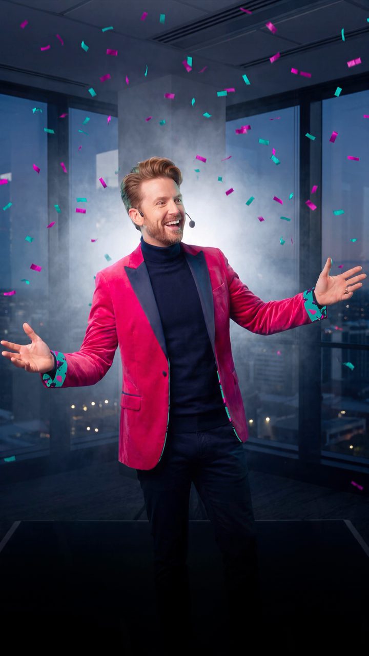 Monty, the AI coach, arms wide in a spotlight in a magenta velvet blazer.
