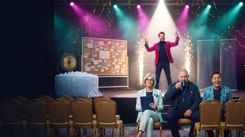 A glitzy hotel ballroom seminar with a fridge-sized vision board and a cold plunge on stage, Monty mid-hype in the spotlight, while Dot, Wilf and Buddy watch from the front row.