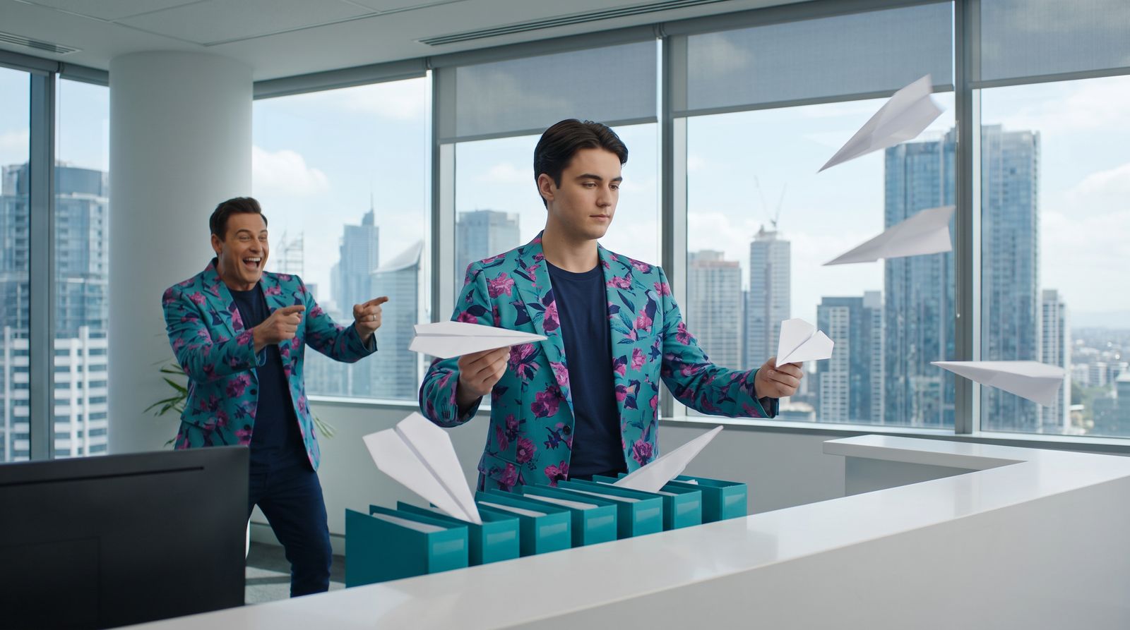 The intake clerk calmly catches paper planes from every direction and files each one into a teal folder