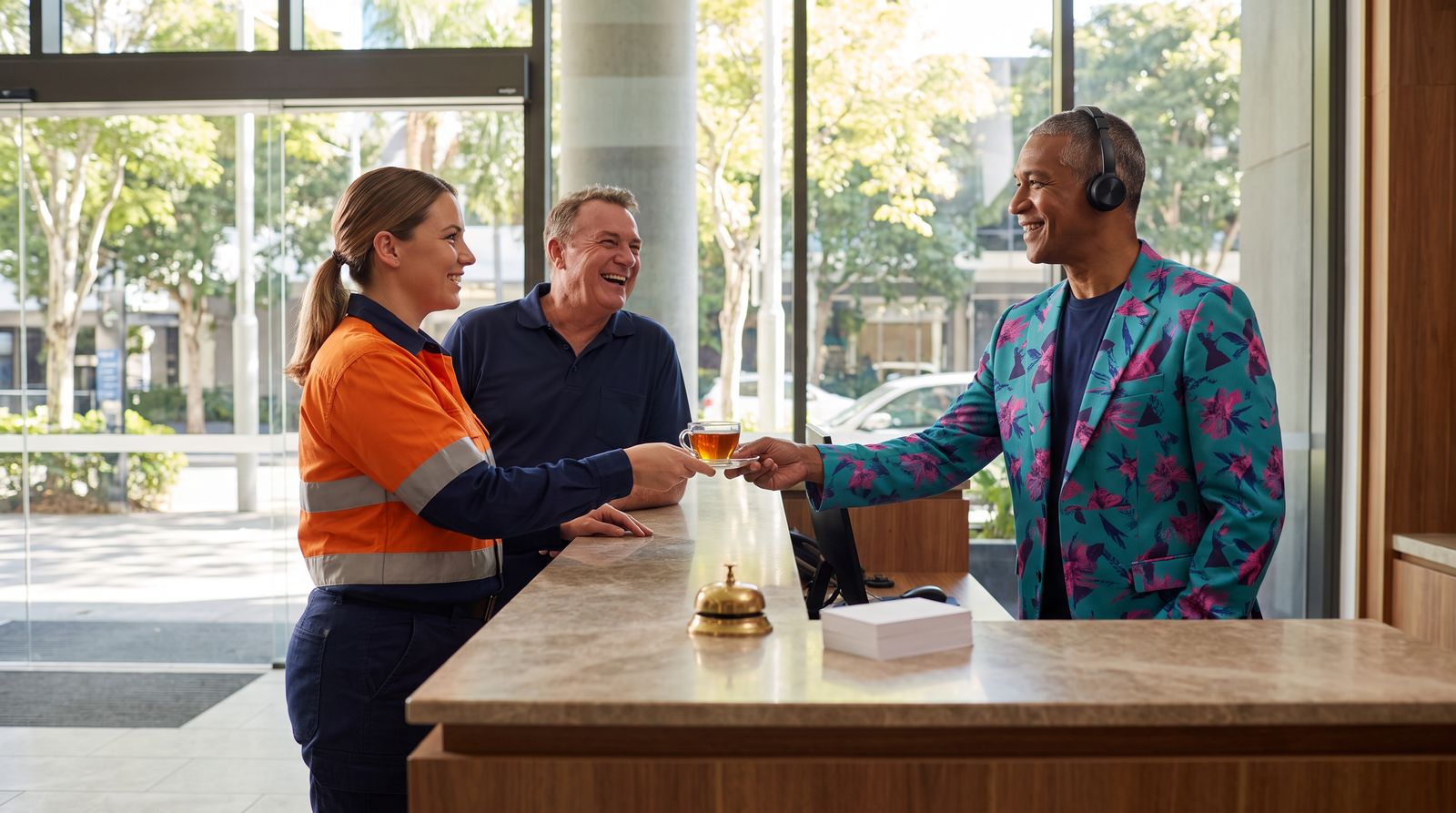 Alfred Care welcomes two small-business staff at a concierge desk and hands one of them a cup of tea
