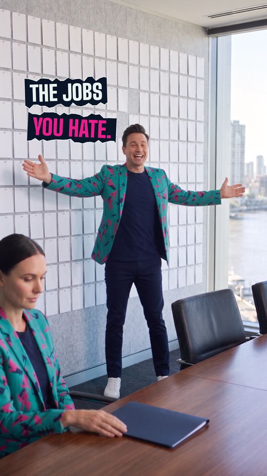 A frame from the film: Buddy (AI) turns from a boardroom wall of blank cards with his arms wide, under the title The jobs you hate, while an AI staffer sits at the table.